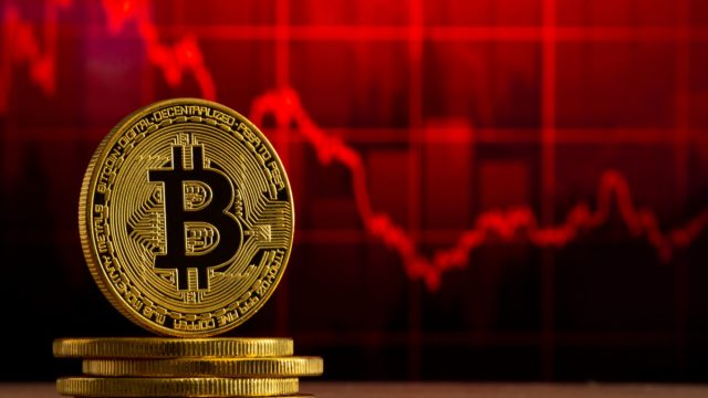 physical bitcoin standing at a wood table in front of a red grap